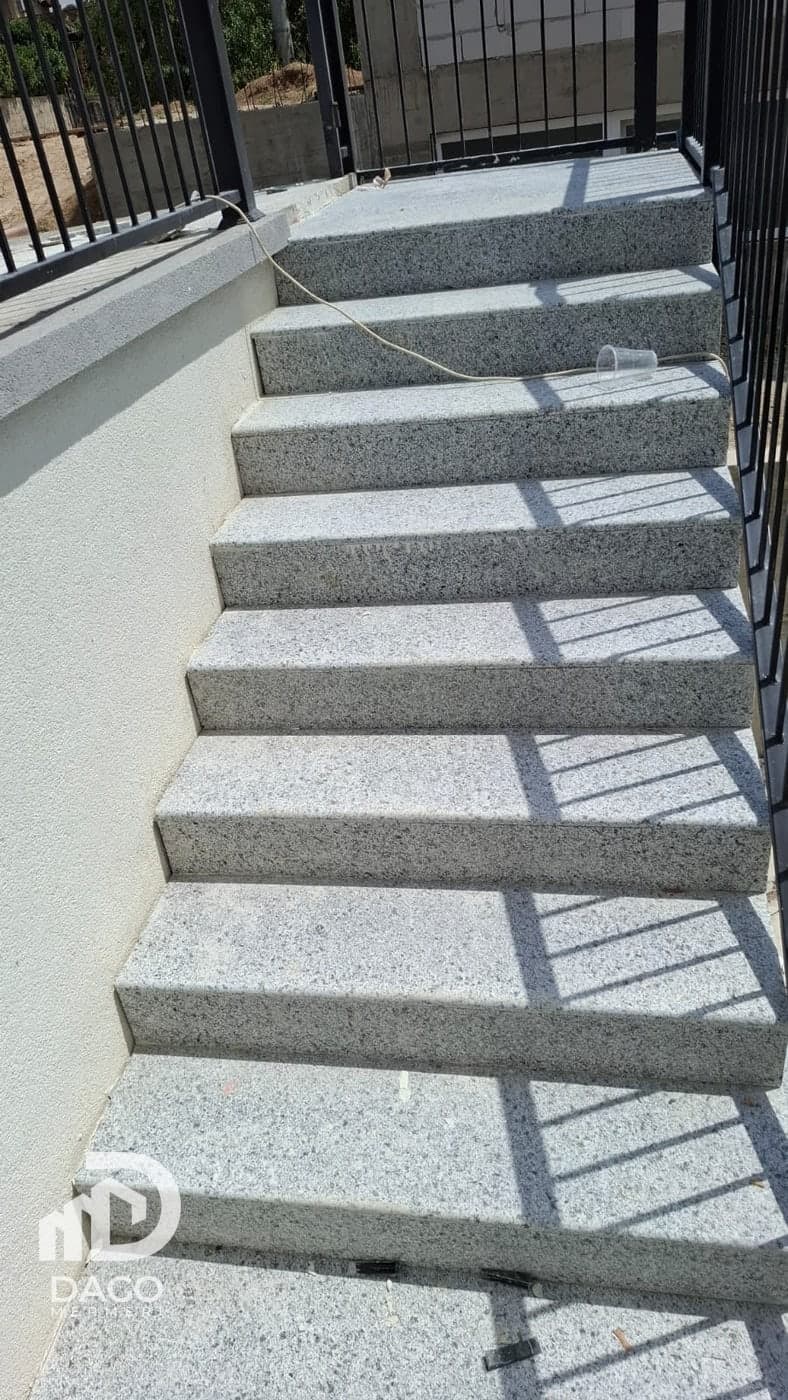 Outdoor rough grey granite stairs along a wall, with a metal railing