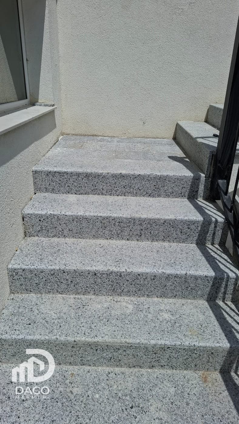 Rough grey granite steps beside a house, with a metal railing
